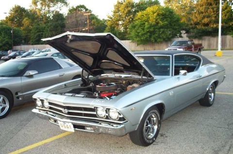 1998 Ford Crown Victoria - A silver 1969 Chevrolet Chevelle SS is parked with its hood open, alongside another car.