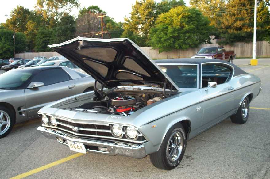 Silver Chevrolet Chevelle SS with black vinyl top and hood raised showing orange V8 engine, three-quarter front view