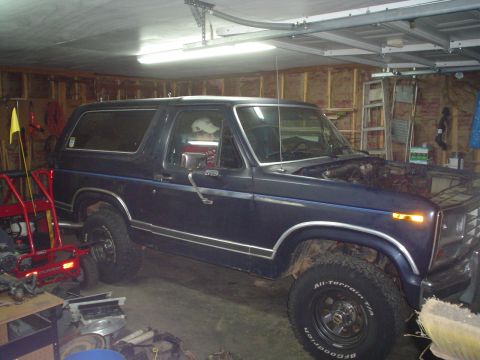 1981 Ford Bronco - This dark blue SUV, likely from the early 1980s, is parked inside a cluttered garage with its hood open.