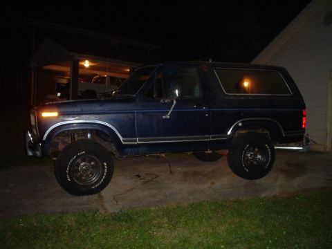 1981 Ford Bronco - A dark blue Ford Bronco is parked on a concrete driveway at night, with a garage visible in the background.