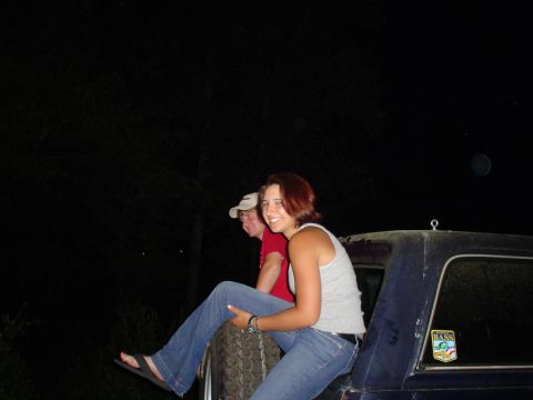1981 Ford Bronco - Two individuals are perched on the rear of a dark blue SUV at night, with a spare tire visible.