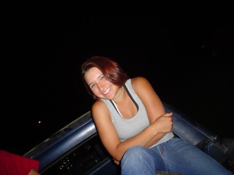1981 Ford Bronco - A woman smiles while sitting in the bed of a pickup truck under a dark night sky.