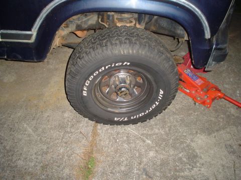 1981 Ford Bronco - A close-up view of a vehicle's wheel and suspension system, with a red jack supporting it.