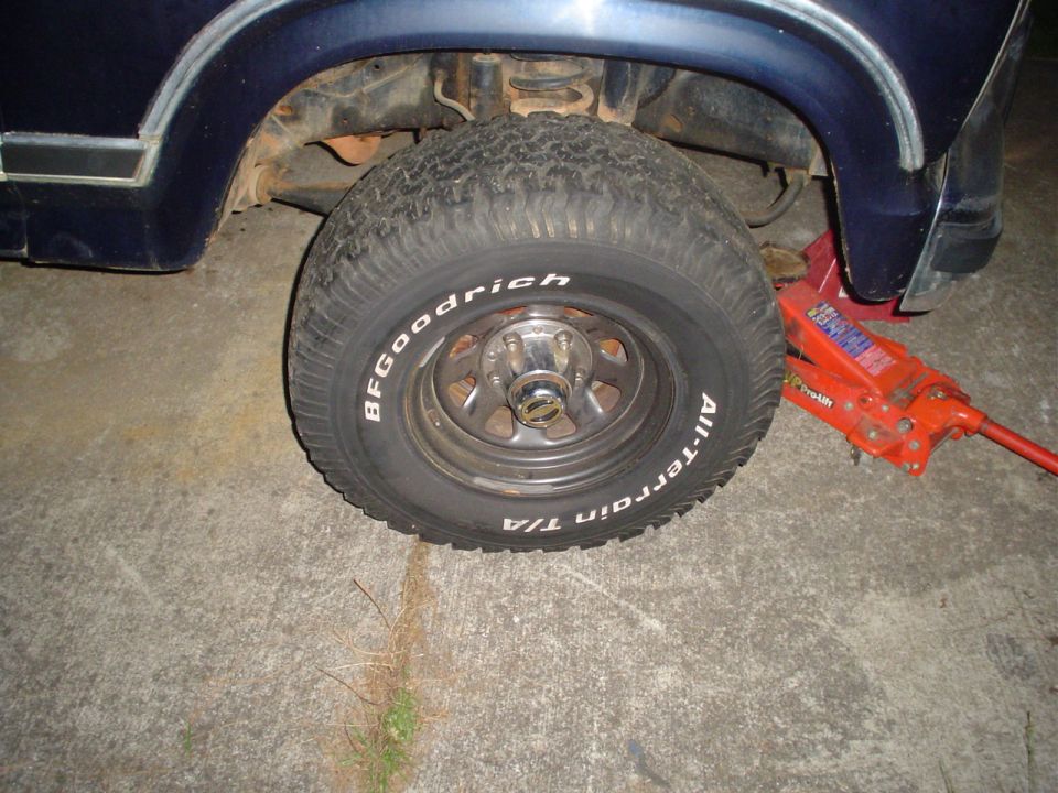 Dark blue vehicle's front wheel and suspension with a red jack underneath