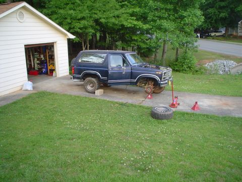 1981 Ford Bronco - A dark blue 1981 Ford Bronco is parked in a driveway with its hood up and front wheel removed, indicating maintenance work.