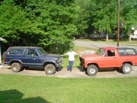 1981 Ford Bronco - Two Ford Bronco SUVs are parked side-by-side in a grassy area with trees in the background.