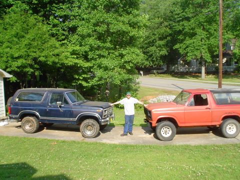 1981 Ford Bronco - A man stands between a blue and an orange Ford Bronco, both appearing to be from the early 1980s.
