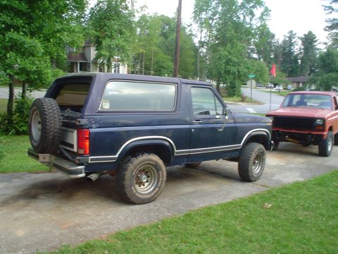 1981 Ford Bronco - A dark blue 1981 Ford Bronco is parked on a driveway next to a red pickup truck.