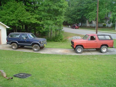 1981 Ford Bronco - Two Ford Broncos are parked side-by-side on a driveway, with a residential street visible in the distance.