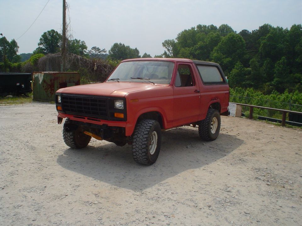red Ford Bronco with aftermarket wheels and tires, parked on dirt