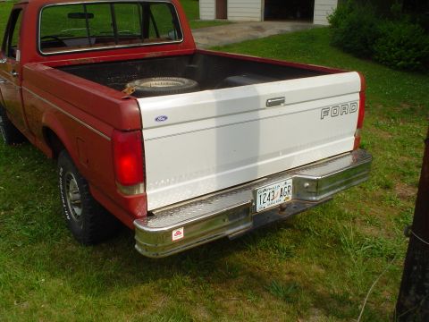 1981 Ford Bronco - A red and white Ford pickup truck is parked on grass, viewed from the rear.