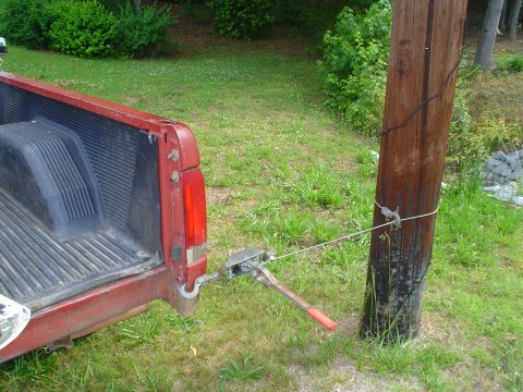 1981 Ford Bronco - A red pickup truck's tailgate is secured to a wooden pole with a winch and rope.