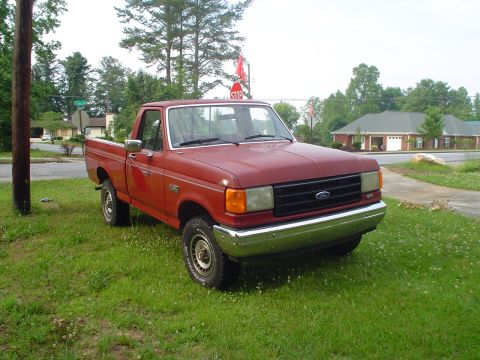 1981 Ford Bronco - This red pickup truck, likely a 1987 Ford F-150, is parked on a grassy area next to a sidewalk.