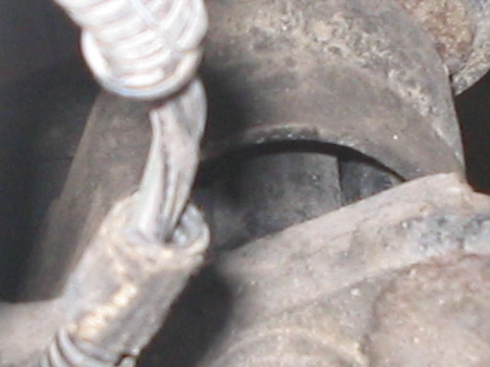 Underbody close-up of rusty axle casting with rubber bushing and coiled brake line