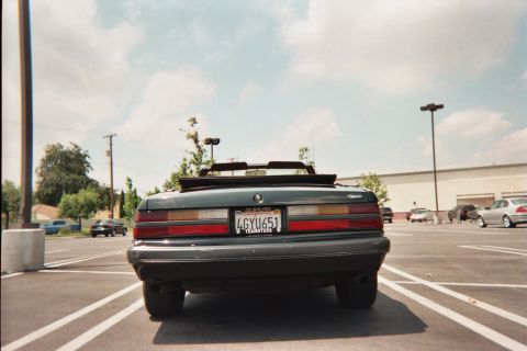 1985 Ford Mustang - Rear view of a dark green convertible parked in a lot, showing its taillights and license plate.
