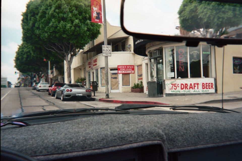 Street corner with a coffee shop and 75-cent draft beer sign seen through a windshield