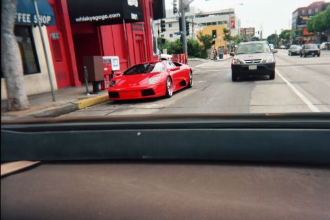 1990 Ford Bronco - red wedge-shaped exotic sports car is parked at the curb outside the Whisky a Go Go as a sedan passes on the street.
