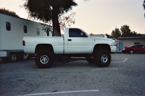 1990 Ford Bronco - white lifted Dodge Ram regular-cab pickup on large tires is parked beside a white enclosed trailer at dusk.