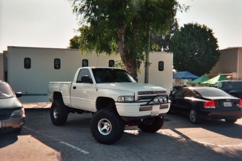 1990 Ford Bronco - white lifted Dodge Ram pickup with a front light bar is parked in a lot beside a white box trailer and other cars.