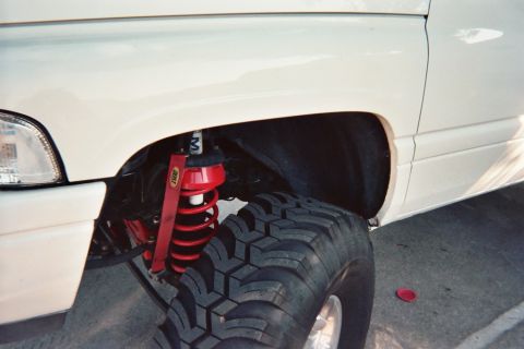 1990 Ford Bronco - close-up shows a red ARB coilover shock and a large knobby mud tire tucked under the fender of a white lifted truck.