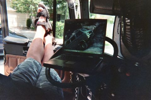 1990 Ford Bronco - Inside a vehicle, a person's sandaled feet rest beside a laptop displaying a photo of a green off-road truck on a hill.