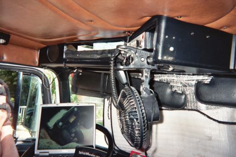 1990 Ford Bronco - overhead vehicle console packed with wiring, a coiled cord and a small electric fan, with a laptop visible below in the cab.
