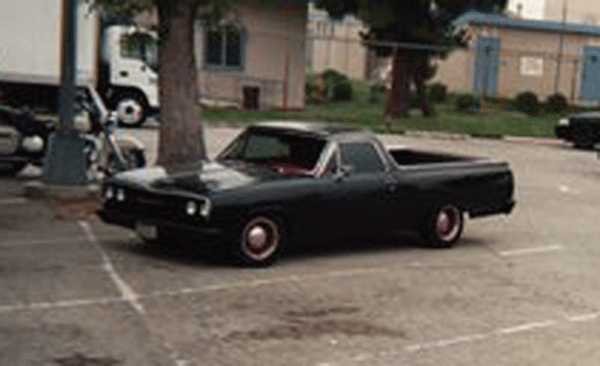 Black car-based pickup, likely a 1960s El Camino, parked in a lot with red steel wheels