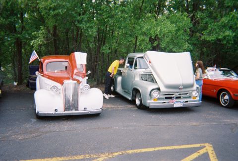 1972 Ford Ranchero - A silver 1956 Ford F-100 pickup truck is displayed with its hood up, alongside other classic vehicles at an outdoor event.
