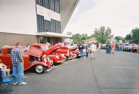 1972 Ford Ranchero - Attendees mill around a car show several vintage red vehicles with hoods open.