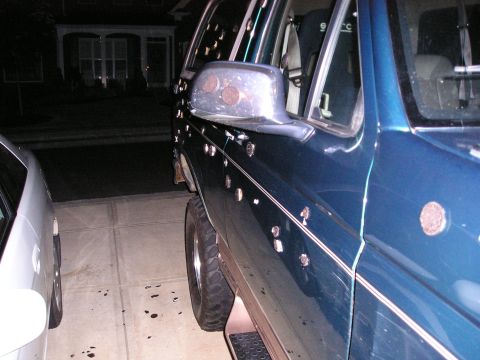 1996 Ford Bronco - This dark blue SUV, likely from the 1990s, shows extensive damage from bullet impacts along its side.