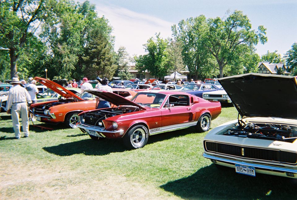 Red Shelby GT350 fastback with white stripes among hood-up muscle cars at a car show