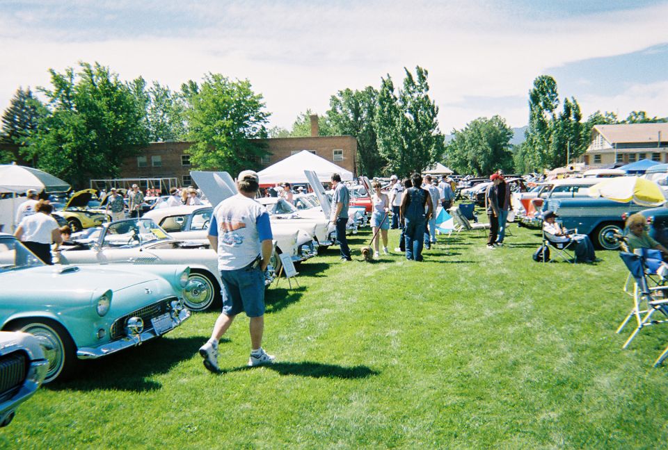 Outdoor car show field with people walking past parked classic cars and Thunderbird