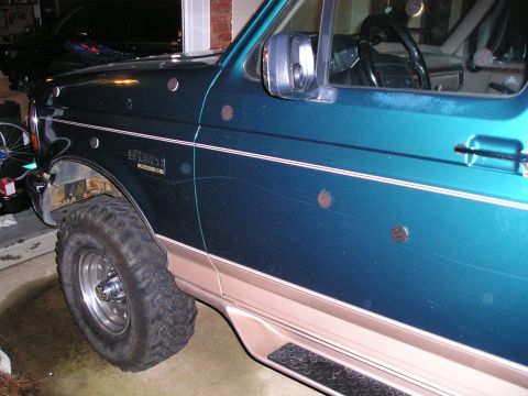 1996 Ford Bronco - The side of a green Ford Bronco is shown, with a dark vehicle parked behind it.