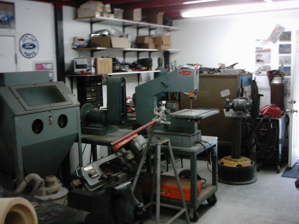 Workshop interior with a sandblaster, band saw, grinder, and shelves of parts