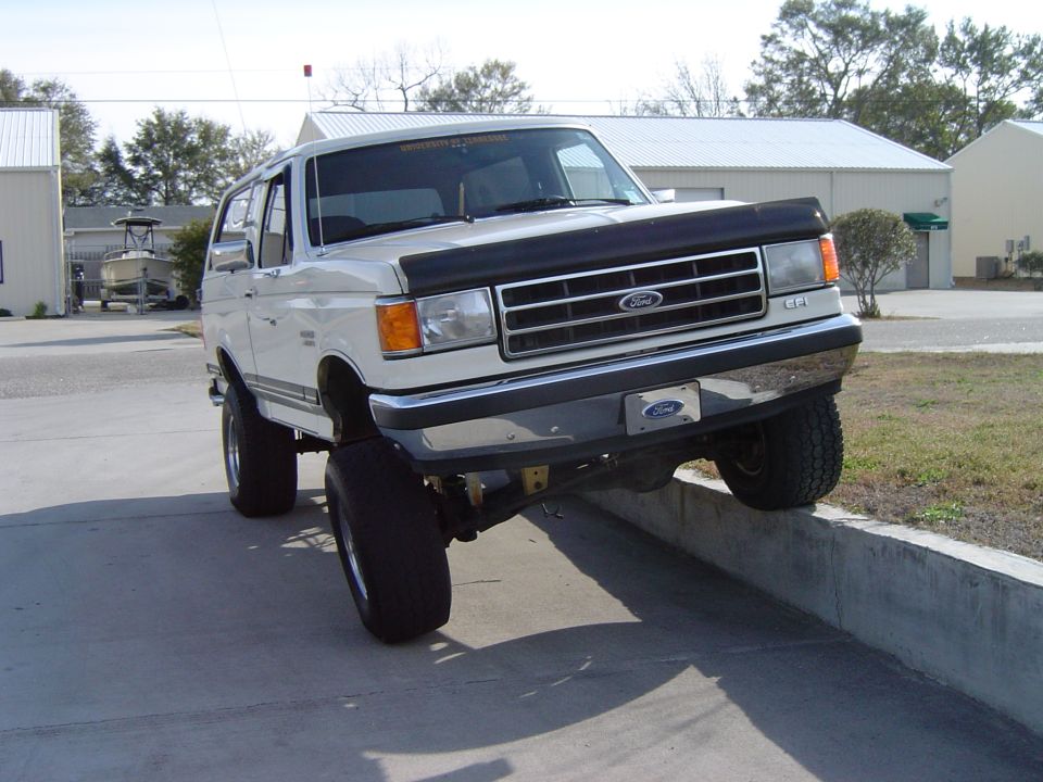 White 1989 Ford Bronco with lifted suspension on a concrete curb