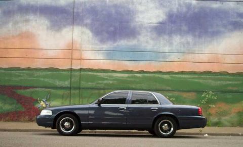 1998 Ford Crown Victoria - A dark blue sedan is parked on the side of the road with a colorful mural in the background.