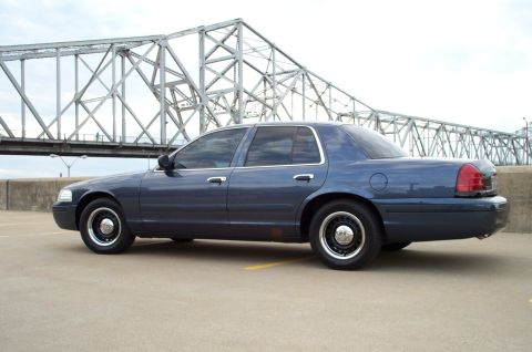 1998 Ford Crown Victoria - A blue 1998 Ford Crown Victoria sedan is parked outdoors with a bridge in the background.