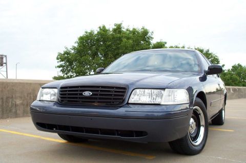 1998 Ford Crown Victoria - A dark blue Ford Crown Victoria is parked in an outdoor lot with trees in the background.