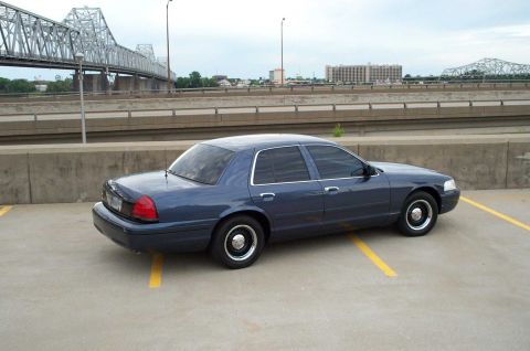 1998 Ford Crown Victoria - Dark blue 1998 Ford Crown Victoria parked in a lot with a bridge in the background.