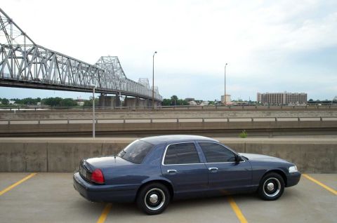 1998 Ford Crown Victoria - A blue sedan is parked in a lot with a large bridge in the background.