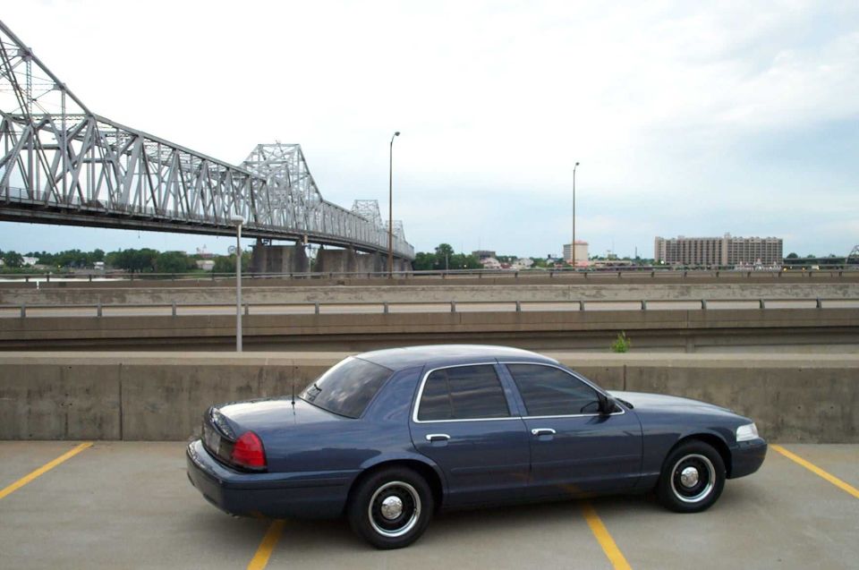 Dark blue Ford Crown Victoria sedan on steel wheels parked near a river bridge