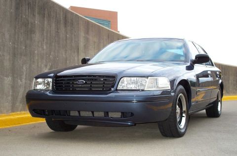 1998 Ford Crown Victoria - A dark blue sedan is parked in front of a concrete wall.