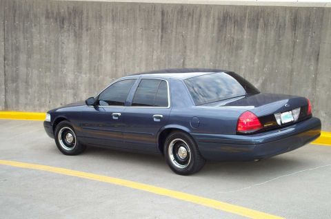 1998 Ford Crown Victoria - A dark blue sedan is parked on a concrete surface with yellow lines, viewed from the rear quarter angle.