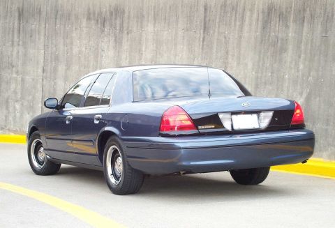 1998 Ford Crown Victoria - Rear view of a dark blue sedan parked against a concrete wall.