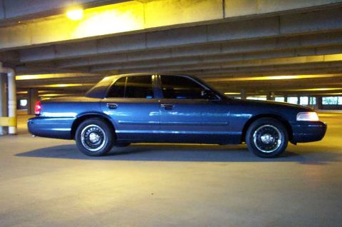 1998 Ford Crown Victoria - Side profile of a blue 1998 Ford Crown Victoria parked in a dimly lit garage.