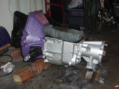 1979 Ford Bronco - A transmission assembly, one part painted purple and the other silver, is supported by wooden blocks.