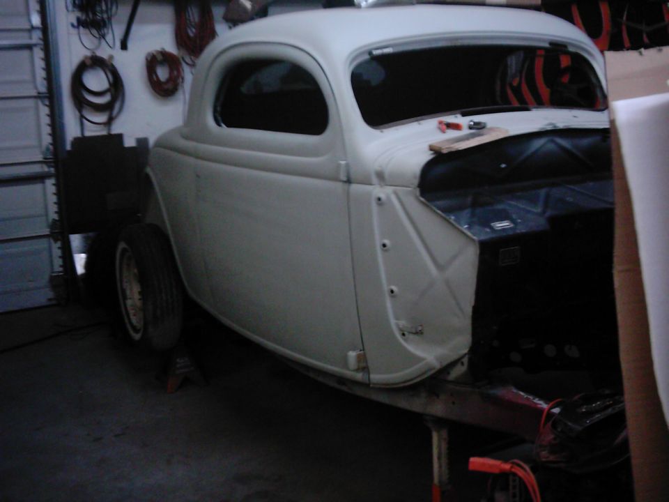 Unfinished coupe body, primer gray, missing hood and fenders, on jack stands in garage