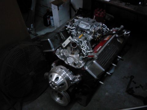 1978 Ford Bronco - A chrome engine assembly sits on a dark surface, with a large fan visible to the left.
