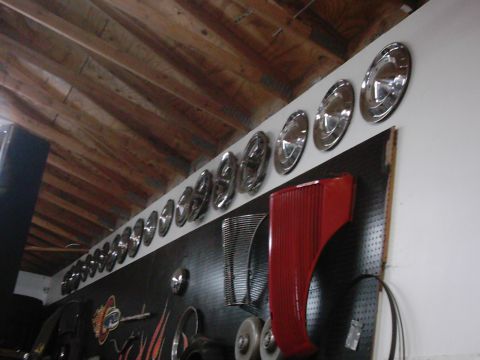 1978 Ford Bronco - Collection of hubcaps and a red fender part mounted on a pegboard wall.