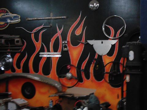 1978 Ford Bronco - A garage wall is decorated with flame graphics and various automotive parts, including steering wheels and hubcaps.